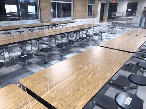 Empty cafeteria with long wooden tables and attached black stools
