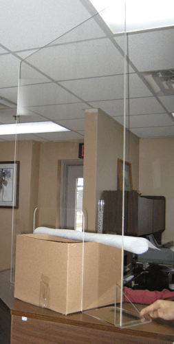 Office cubicle with a cardboard box and rolled white item on the desk, partition panels in front of it