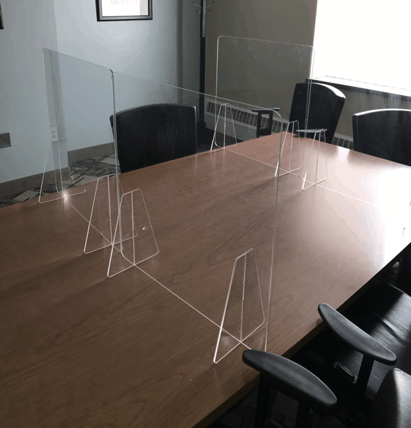Conference room table with clear acrylic desk dividers and black chairs around it