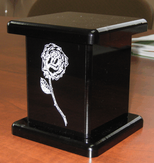Black decorative keepsake box with a white rose design on the front, sitting on a wooden table.