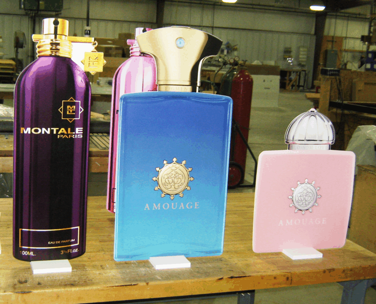 Three luxury perfume bottles on a wooden table in a warehouse, including purple, blue, and pink bottles.
