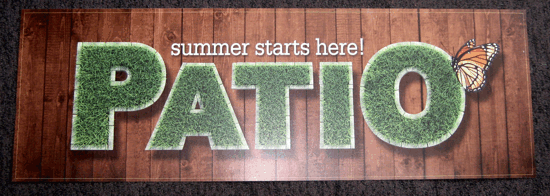 Wooden sign reading “summer starts here!” above large green letters spelling “PATIO” with a leaf accent.