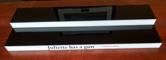 Black rectangular device on a white base with a small label in front on a display stand