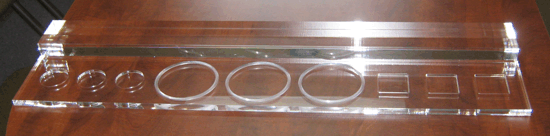 Clear acrylic tray with assorted metal rings and circular cutouts on a wooden surface.