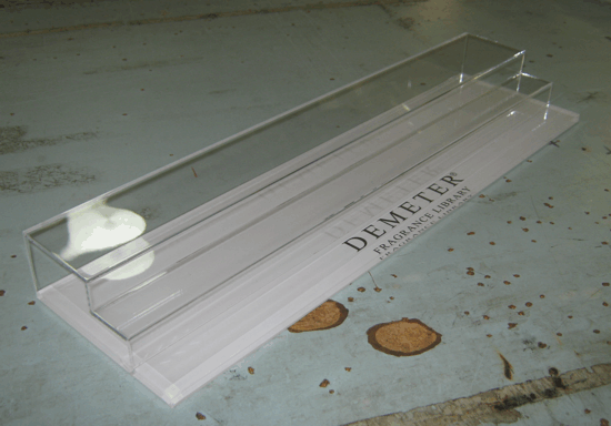 Clear plastic display stand labeled “DEMBER” on a speckled tabletop