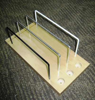 Wire rack/book holder with four metal dividers on a light wooden base, on a carpeted floor