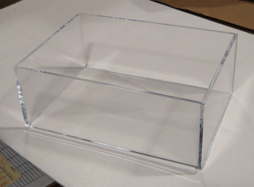 Clear acrylic display box on a white surface, viewed from above at an angle.