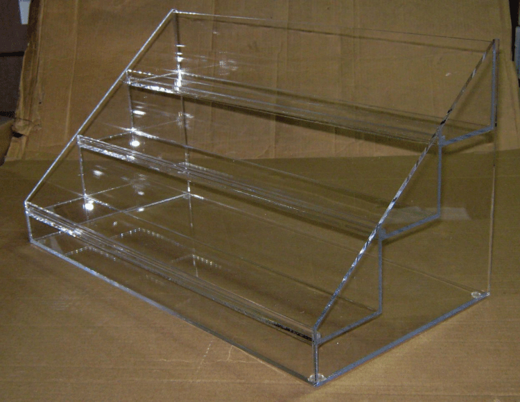 Clear acrylic countertop display rack with three stepped shelves on a brown surface
