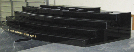 Black tiered display stand with a few clear blocks on a gray surface, viewed from the side