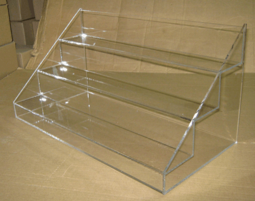 Clear plastic three-tier display riser on a cardboard box, viewed at an angle