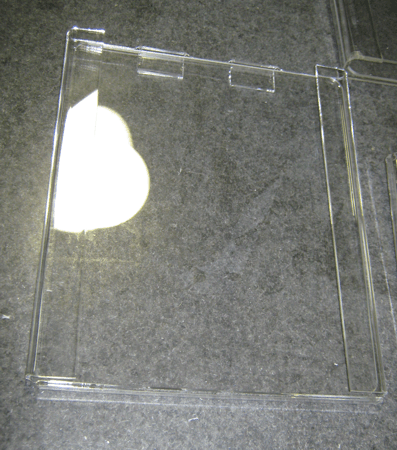 Clear plastic CD case on a dark textured surface, with a bright white glare on the left side.