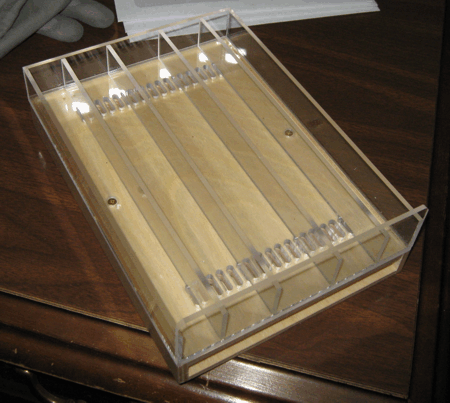 Clear acrylic tray on a wooden table, with small metal balls lined up in a row at one end.