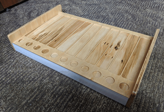 Wooden tray with raised sides and circular cutouts, resting on a gray carpet.