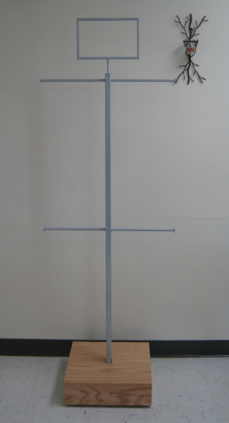 Metal stand with a rectangular top and side branch, mounted on a wooden base against a wall.