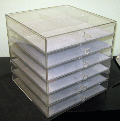 Clear acrylic drawer organizer with six white trays on a dark surface