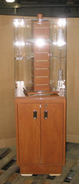 Wooden cabinet with a clear display case on top, holding stacked brown blocks in a warehouse-like setting
