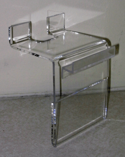 Clear acrylic over-toilet shelf with raised lips, shown against a wall on a carpeted floor.