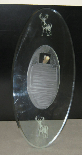 Oval glass plaque with etched figures and a ribbed silver center plate on a dark background