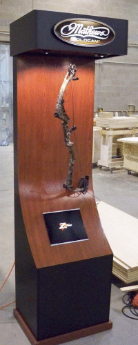 Tall wooden display kiosk with a mounted black prosthetic limb in a workshop
