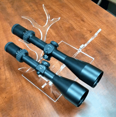 Two black riflescopes on a wooden table, one larger than the other.