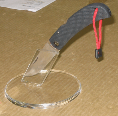 Kitchen knife with transparent blade and black handle resting on a clear glass plate on a table