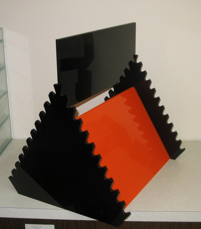 Black and orange accordion-style display stand on a white surface with a screen behind it
