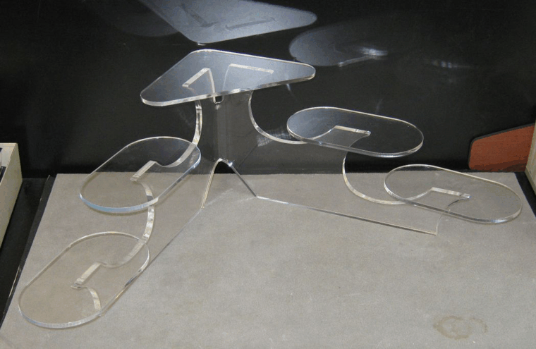 Clear acrylic tiered table with oval shelves on a floor against a dark background