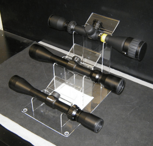 Three black rifle scopes displayed on clear acrylic stands in a showcase