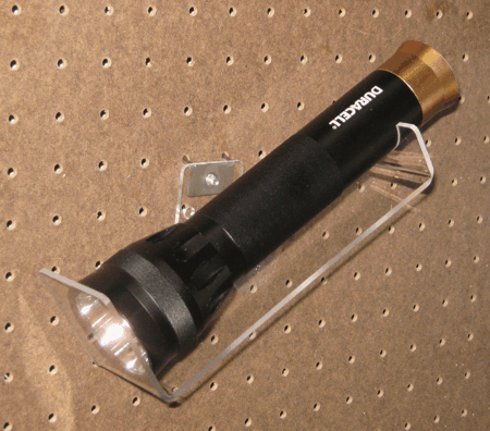 Black flashlight with gold tail cap mounted on a clear wall display bracket.