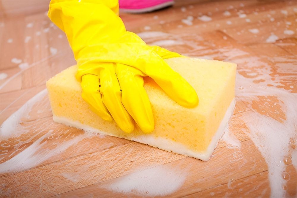 A Person Wearing Yellow Gloves Is Cleaning A Wooden Floor With A Sponge — Crystal Clear In Armidale, NSW
