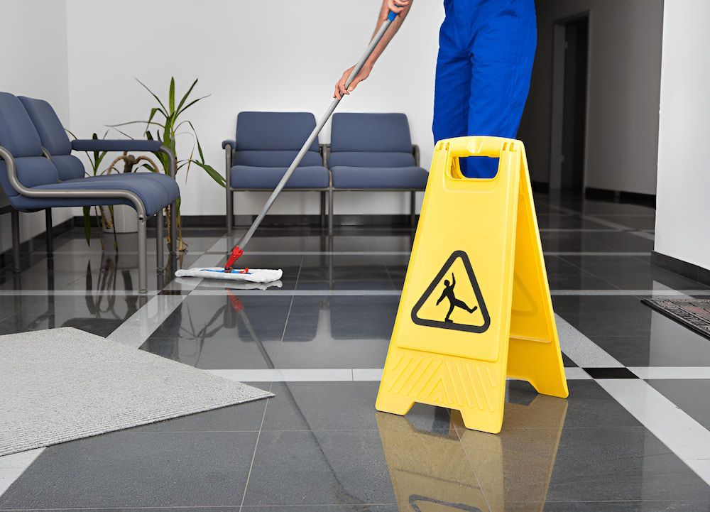 A Man Is Mopping The Floor Next To A Yellow Caution Sign — Crystal Clear In Guyra, NSW