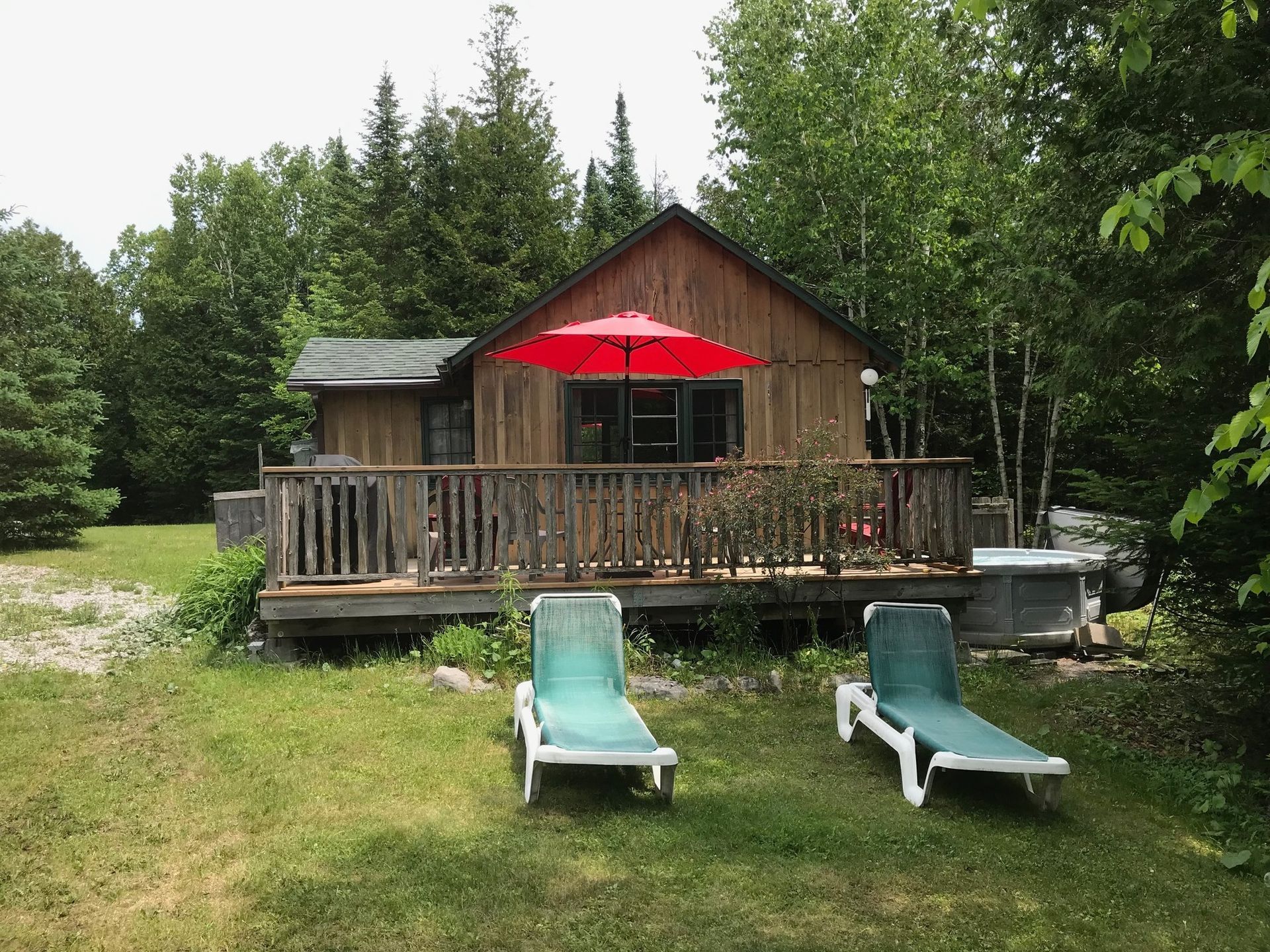 A small wooden cabin with a red umbrella and two lounge chairs in front of it.