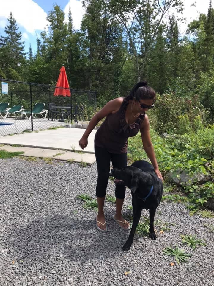 A woman is standing next to a black dog.
