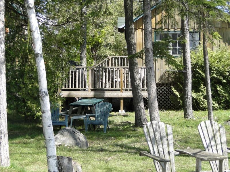 A house with a deck is surrounded by trees and chairs