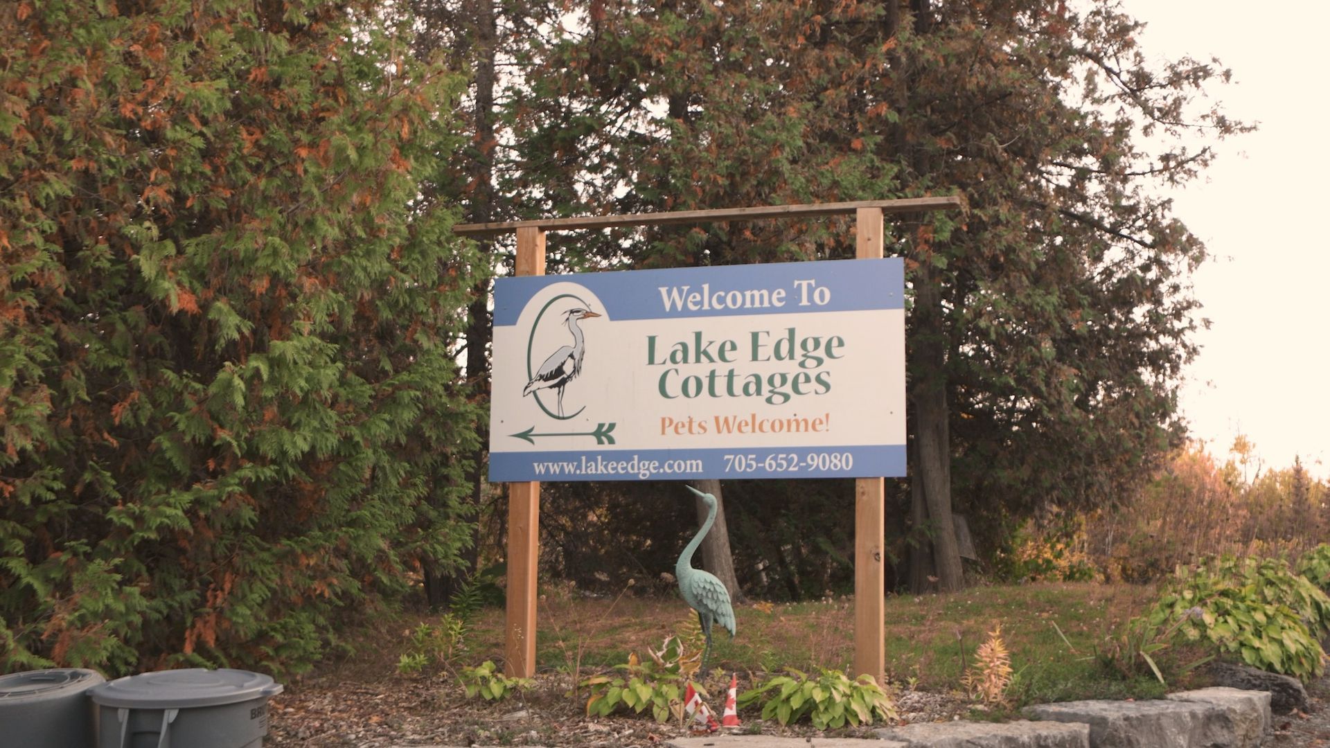 Sign for Lake Edge Cottages, blue and white text on brown posts, with heron statue.