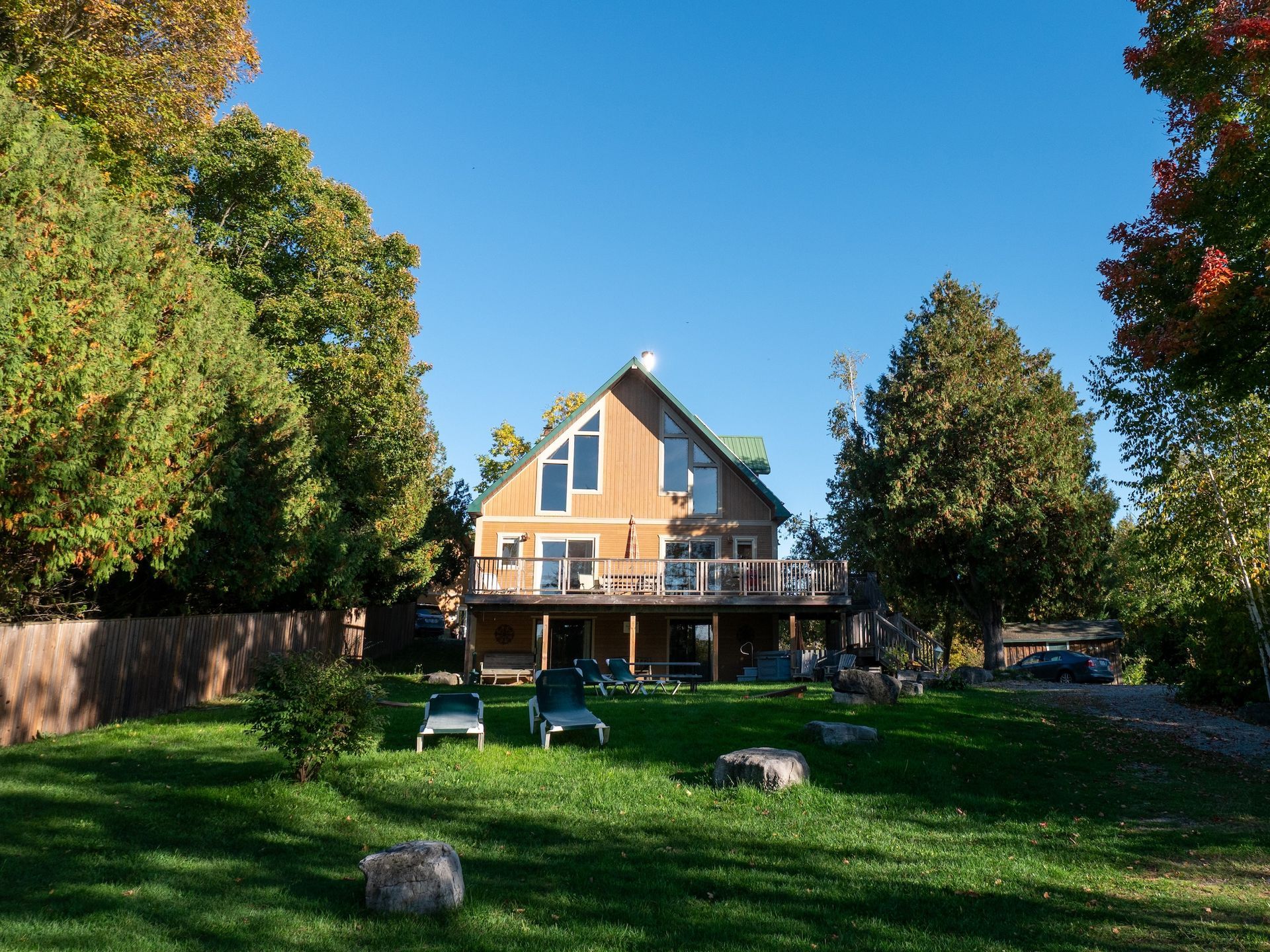 Wooden house with deck, lawn, trees under a blue sky.