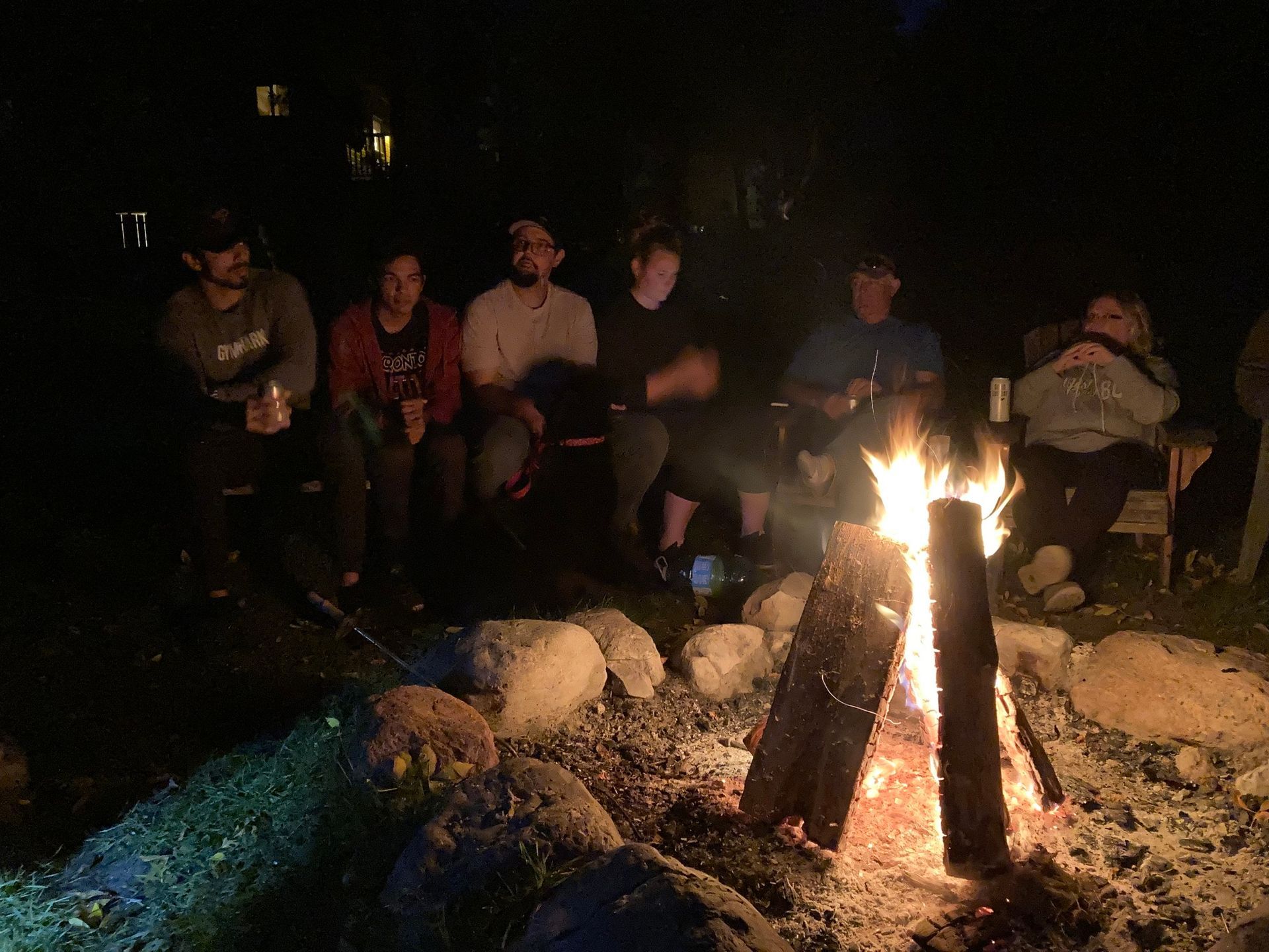 A group of people are sitting around a campfire at night.