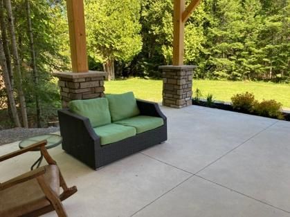 A couch with green cushions is sitting on a patio with a rocking chair.
