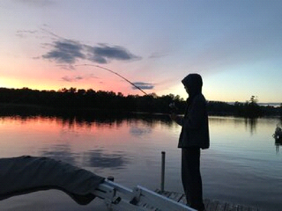 A man is fishing on a lake at sunset.