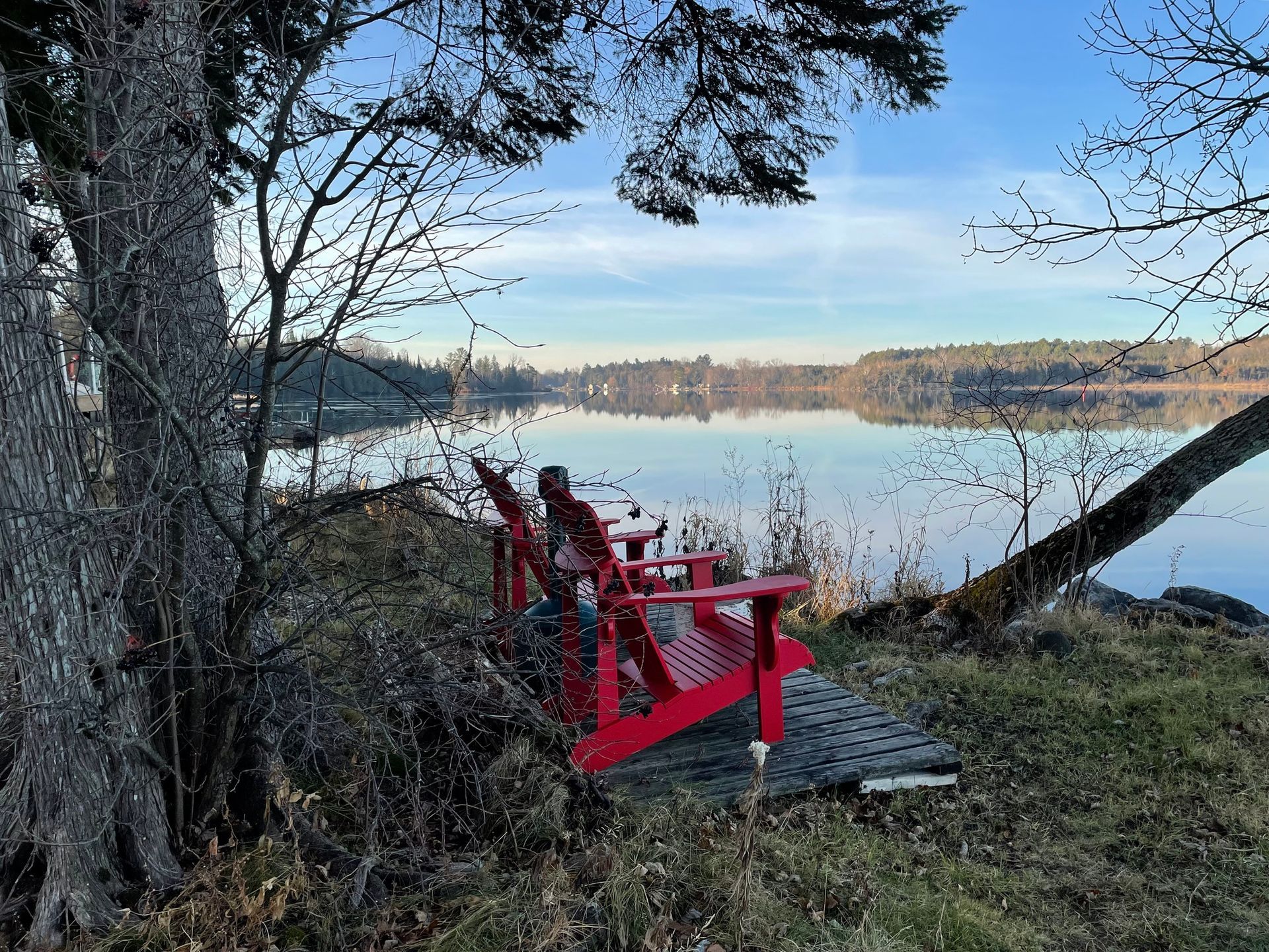 A red chair is sitting on the shore of a lake.