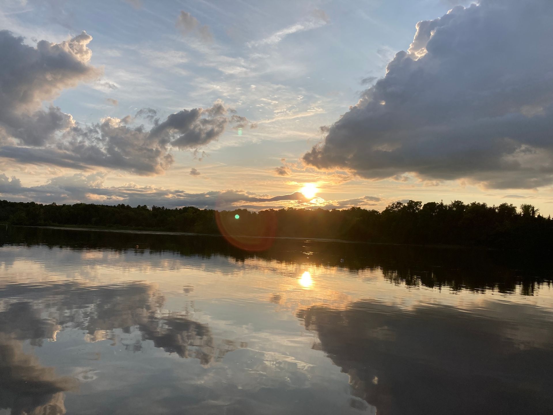 The sun is setting over a lake with clouds reflected in the water.