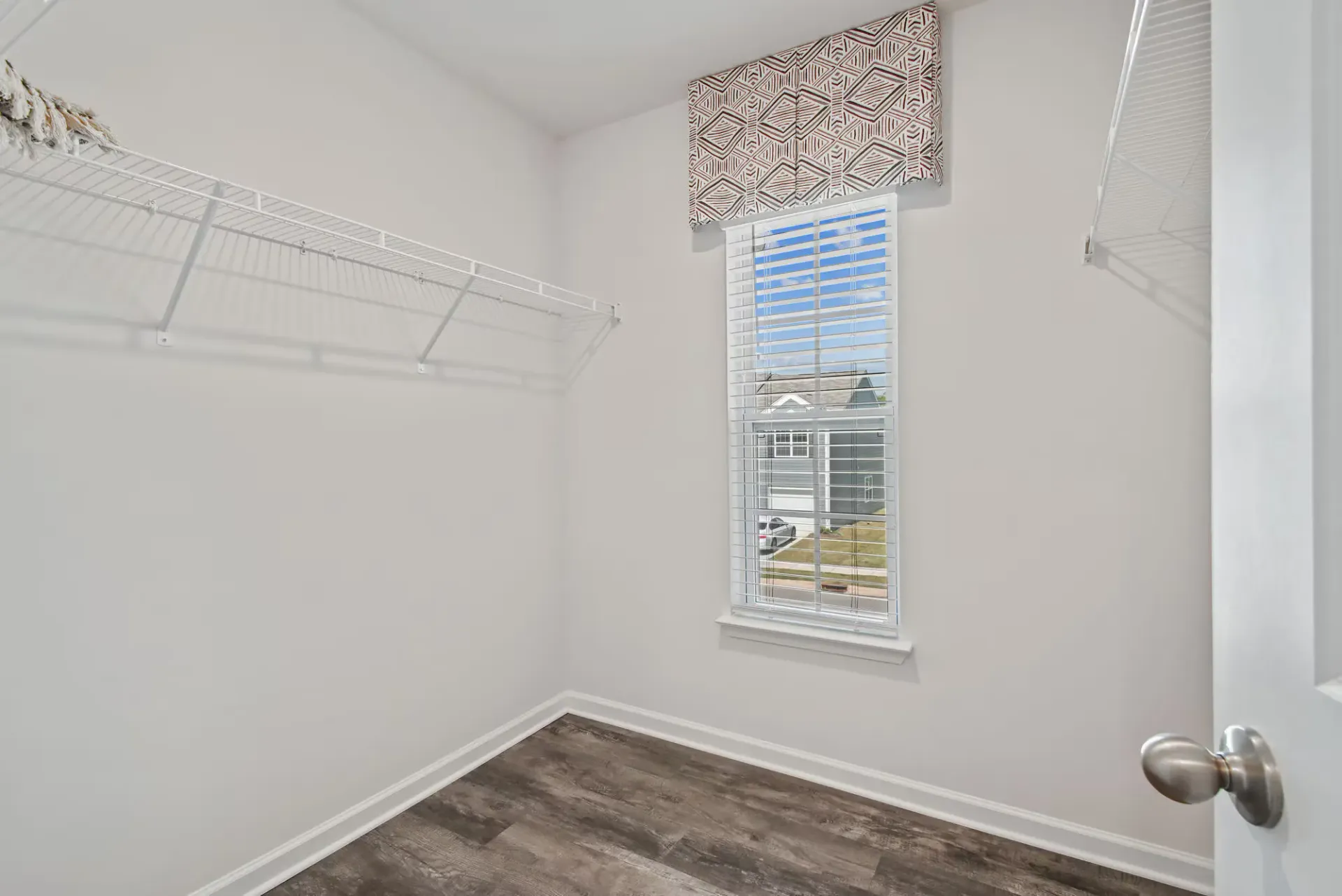 Walk-in closet with wire shelving along both walls and a window with blinds.