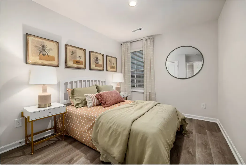Cozy bedroom in an apartment with a bed, two nightstands, lamps, and a round mirror.