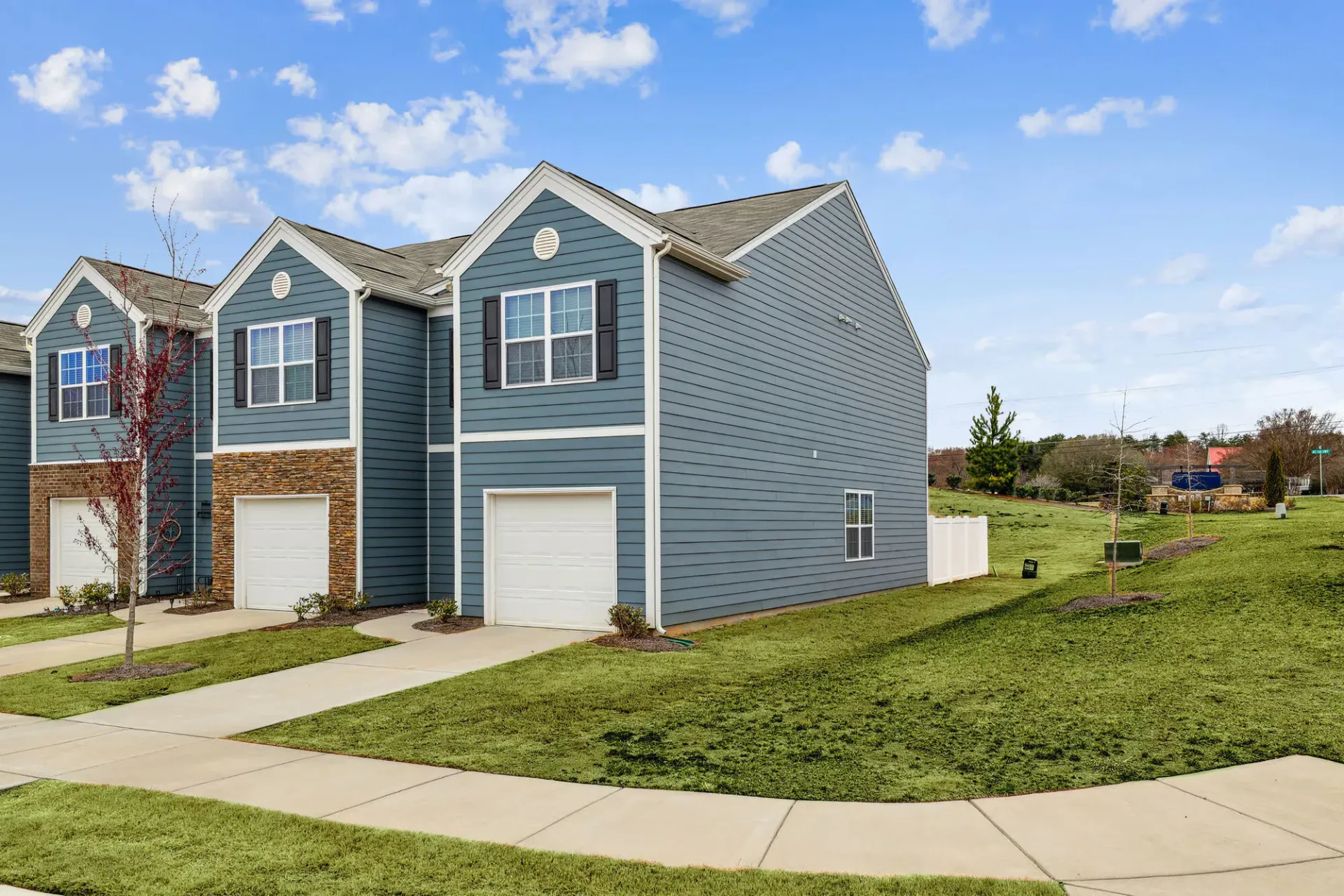 Blue townhouse-style apartment building exterior with attached garages and landscaped lawn.