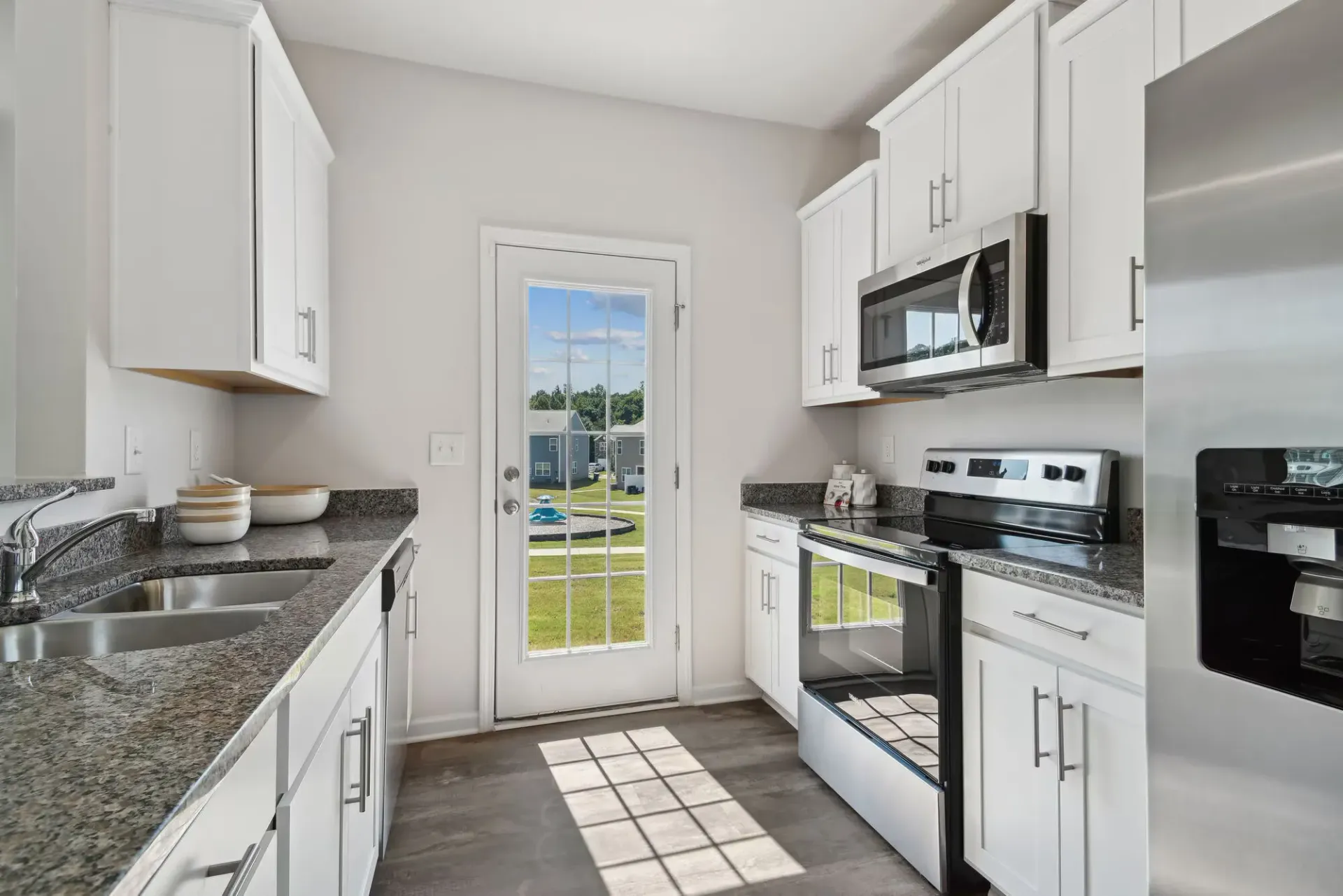Bright white kitchen with granite countertops, white cabinets, stainless steel appliances, and a glass door.