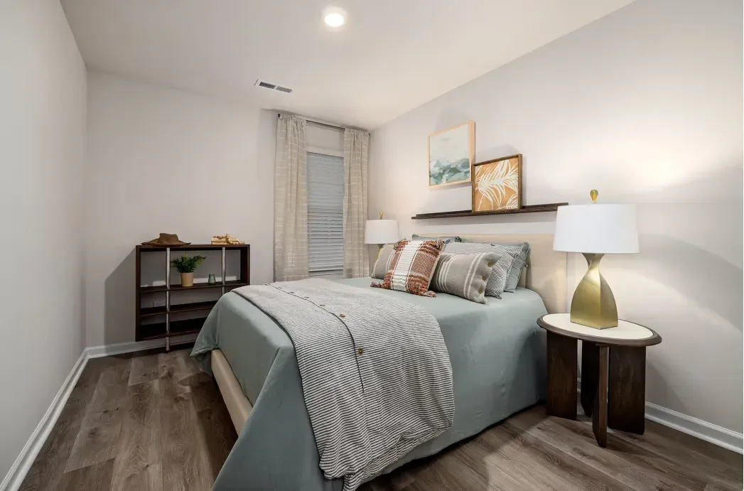 Bedroom in a modern apartment with a bed, nightstands, lamps, and wall art.