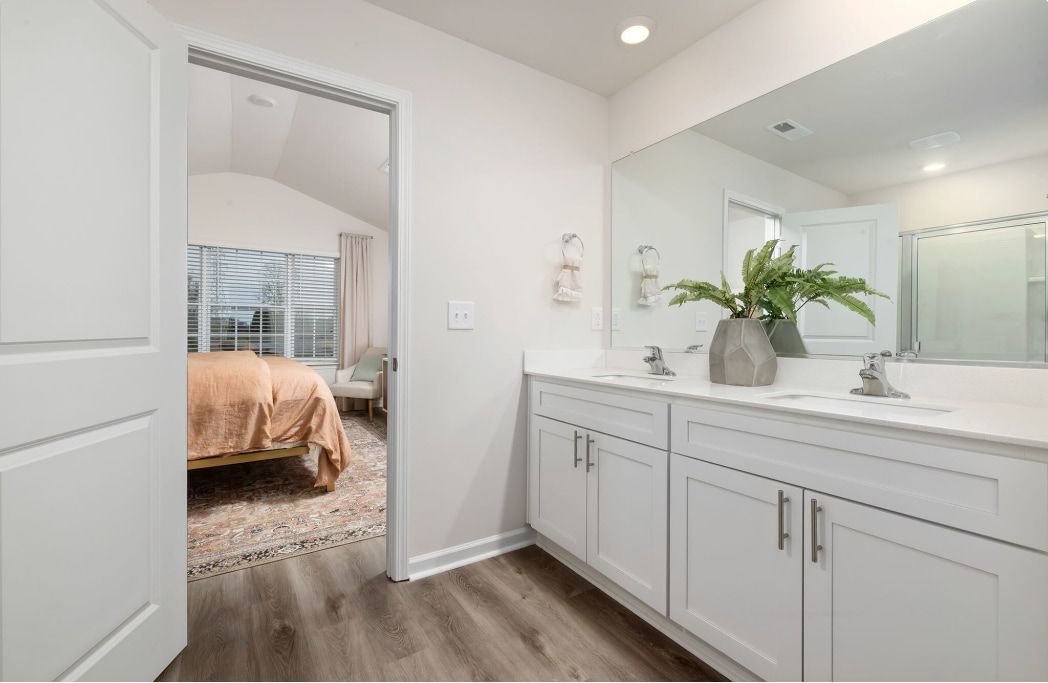Bathroom vanity with double sinks, white cabinets, and a doorway to a bedroom.
