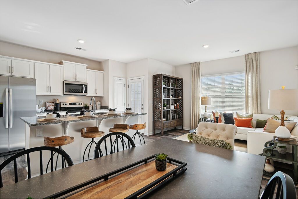 Open-concept kitchen and living area with island, bar stools, and a sofa under a window.