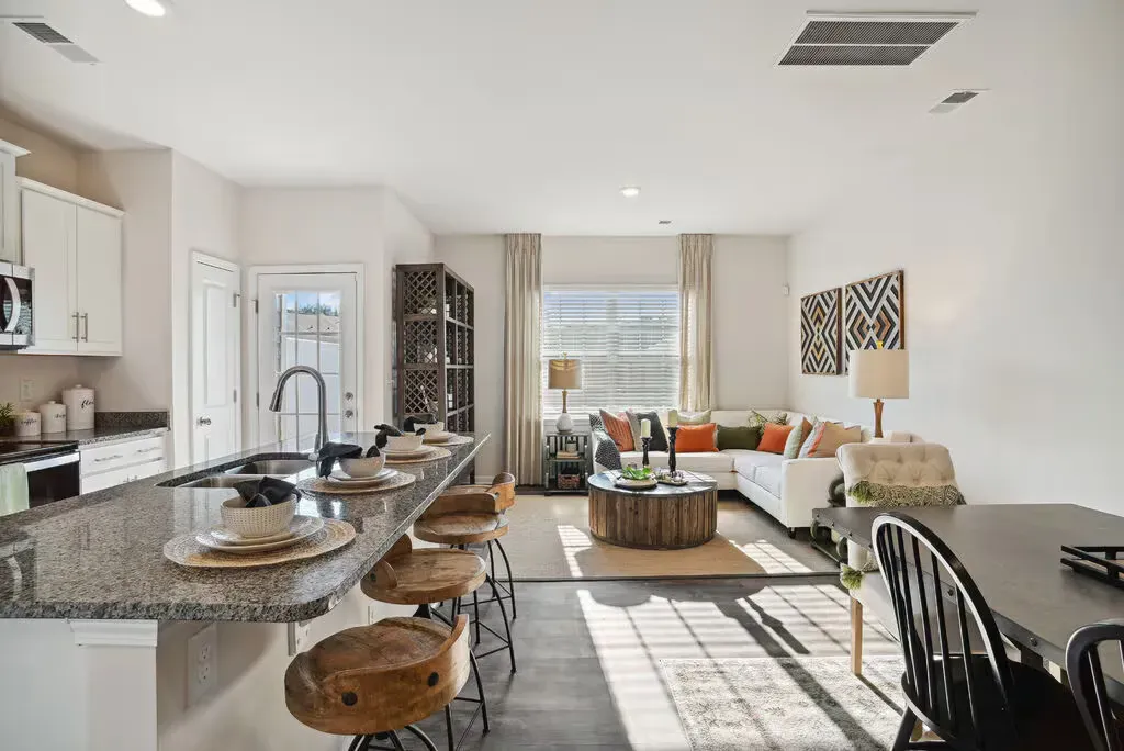 Open-concept kitchen with granite island and bar stools flowing into a bright living room.