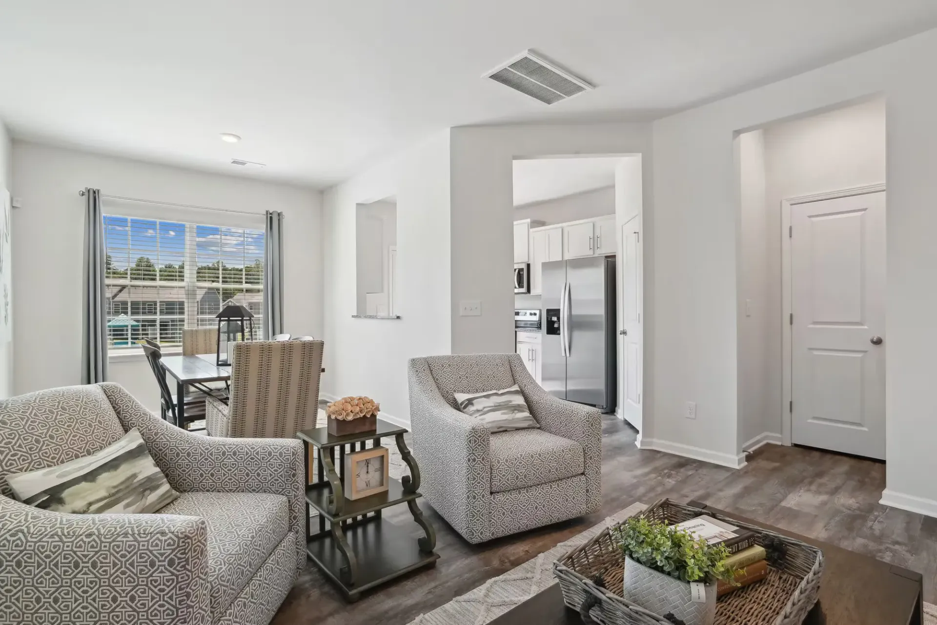 Bright open-concept living room with two patterned armchairs, a coffee table, and a view into the modern kitchen.